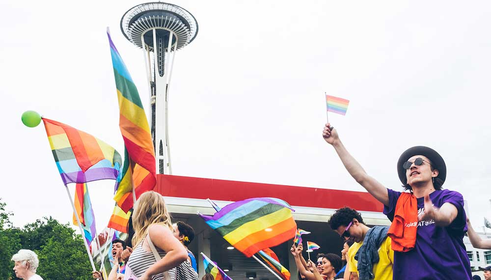 people carrying a pride flags in front of space needle